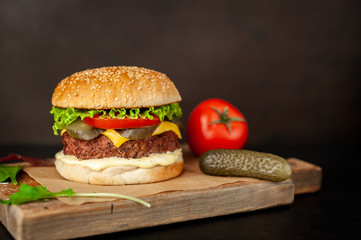 Homemade hamburger with lettuce, tomato, cheese and cucumber on a cutting board