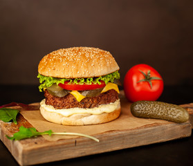 Homemade hamburger with lettuce, tomato, cheese and cucumber on a cutting board