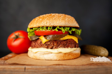 Homemade hamburger with lettuce, tomato, cheese and cucumber on a cutting board