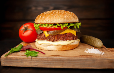 Homemade hamburger with lettuce, tomato, cheese and cucumber on a cutting board