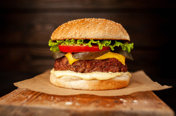 Homemade hamburger with lettuce, tomato, cheese and cucumber on a cutting board