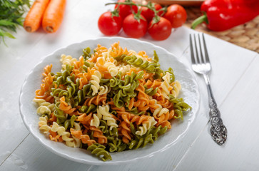 Multicolored pasta with vegetable on wooden background ve vegetables