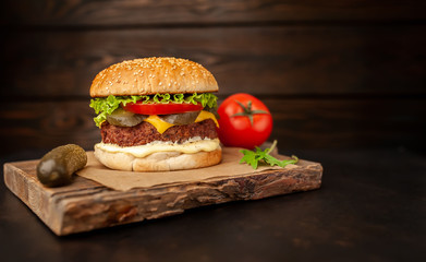 Homemade hamburger with lettuce, tomato, cheese and cucumber on a cutting board