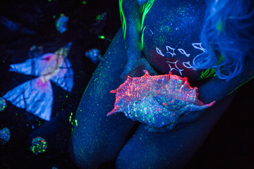 seashell in the neon light in the hands of a pregnant girl