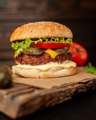 Homemade hamburger with lettuce, tomato, cheese and cucumber on a cutting board