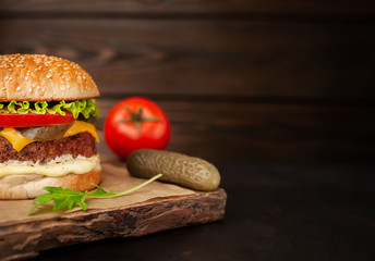 Homemade hamburger with lettuce, tomato, cheese and cucumber on a cutting board