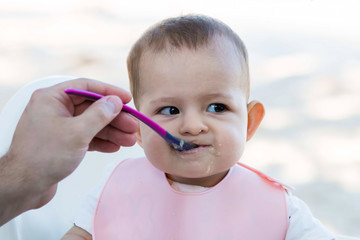 Beautiful baby eating mashed. Spoon  feed outdoor, Eats porridge on the beach