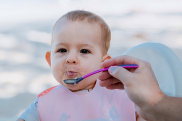 Dad feeds the baby with a spoon of porridge. Outdoors. The child was messing but happy