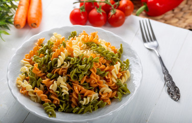 Multicolored pasta with vegetable on wooden background ve vegetables