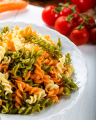 Multicolored pasta with vegetable on wooden background ve vegetables