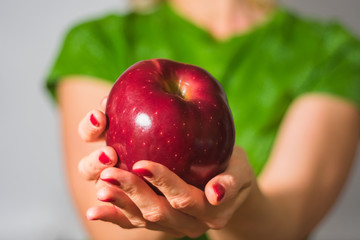 The girl holds a big red apple in his hands. Apple and fingers in focus. Body girl in defocusing