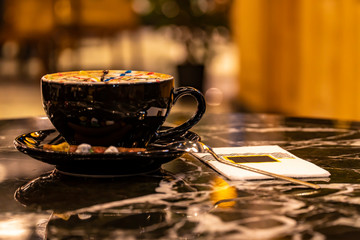 Hot Cappuccino coffee with colorfull caramel motif art floating on top and coffee beans. Coffee break at retro style coffee shop.