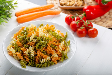 Multicolored pasta with vegetable on wooden background ve vegetables