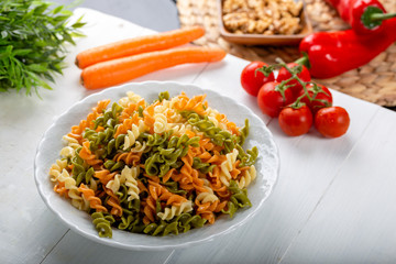 Multicolored pasta with vegetable on wooden background ve vegetables