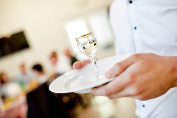 waiter's hands hold a plate on which is a glass of vodka