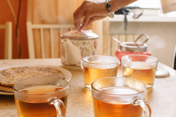 Woman pours hot tea from ceramic teapot into transparent glass cups