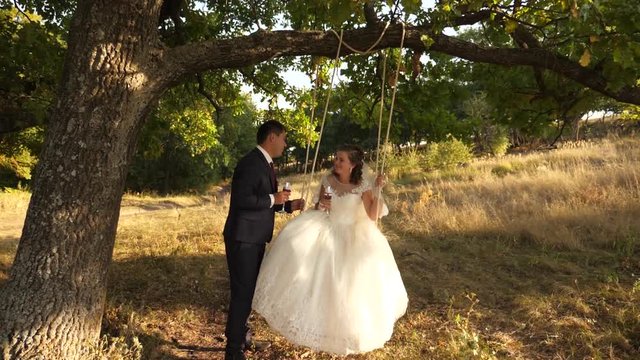 Happy groom swinging on a swing the bride in the park in summer. boy and girl swing on a branch of an oak in summer forest. happy family concept. teamwork of a couple in love.