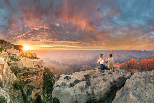 Man and woman sit on the edge of rim talking about future and watching the Grand Canyon sunset