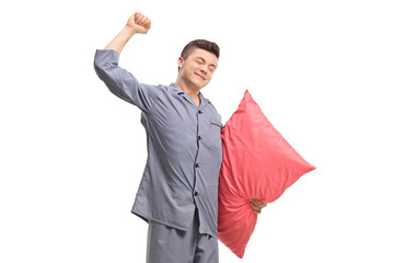 Young man in pajamas holding a pillow and stretching himself