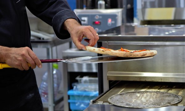 Ready Italian pizza on thin dough, chef pulls out of the oven, equipment for the production. 
