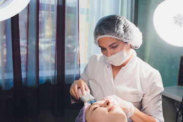 Hardware cosmetology. Beautician makes chromotherapy ultrasound cleaning the client's face. Skin...