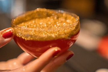 Golden cocktail glass at the bar. Young women's hand holding a martini glass with a golden stardust...