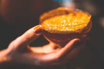 Golden cocktail glass at the bar. Young women's hand holding a martini glass with a golden stardust...