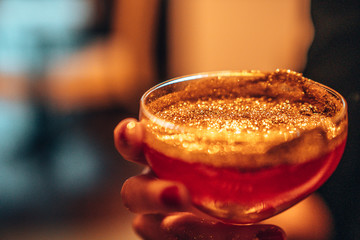Golden cocktail glass at the bar. Young women's hand holding a martini glass with a golden stardust...