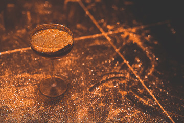 Golden cocktail glass at the bar. Young women's hand holding a martini glass with a golden stardust...