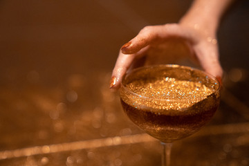 Golden cocktail glass at the bar. Young women's hand holding a martini glass with a golden stardust...