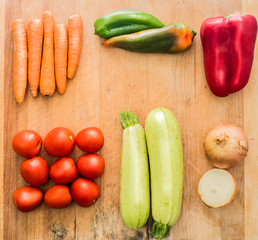 Tabla de madera con varias verduras encima. Zanahorias, pimiento rojo y verde, tomates rojos, calabacín verde y cebollas