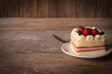 strawberry leyer cake topping strawberry putting on the white plate on the wood table background there is fork placed back side.