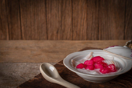 Thapthim krop, mock pomegranate seeds in coconut and syrup in the white bowl on the wood table there is spoon ceramic placed in front of.