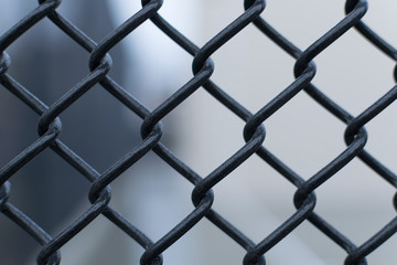 Black chain link fence against a smooth blurred out background, close-up