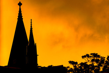 Obraz premium Silhouette of a church steeple and some high tree-branches, against a bright yellow fiery-looking sky during sunset, Harlem, New York City, USA