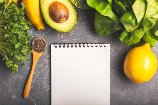 Diet, nutritoon plan, shopping list or recipe concept. Greens, spinach, avocado, banana and lemon on moody background. Healthy eating, diet and vegetarian. Horizontal shot. Copy space for your text.