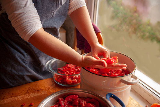 woman cook in apron prepares tomatoes in saucepan, rubs through sieve and prepares tomato juice. Female hands closeup.