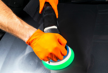 Car polish wax worker hands applying protective tape before polishing. Buffing and polishing car. Car detailing. Man holds a polisher in the hand and polishes the car. Tools for polishing