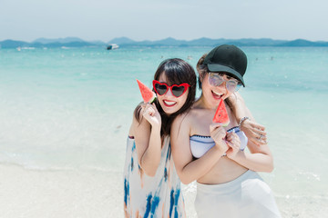 Full body portrait of two young women friends laughing and enjoy on the beach,In the hands holding a fruit.