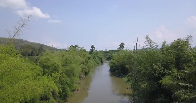 Forward drone motion above a remote rural river with overgrown vegetation in a tropical humid climate with an ascent and aerial overview of dense woodland and trees