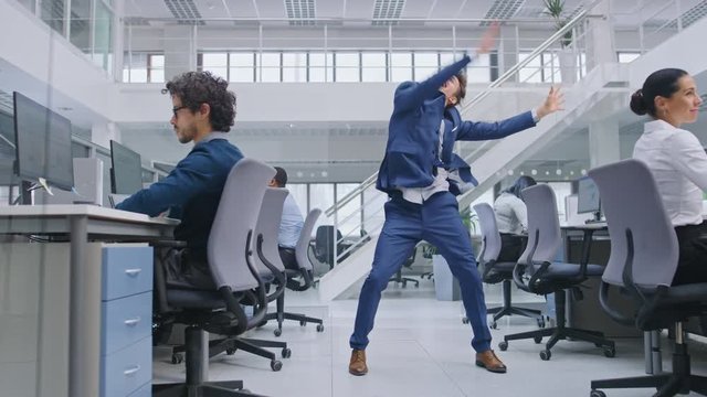 Young Cheerful Handsome Business Manager Wearing a Suit and Tie Dancing in the Office. Diverse and Motivated Business People Work on Computers in Modern Open Office.