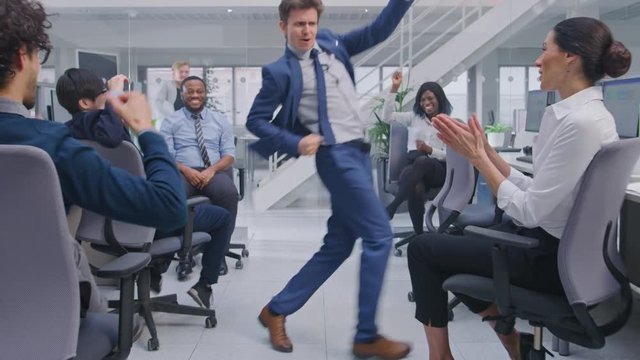 Young Happy Business Manager Wearing a Suit and Tie Dancing and Giving High Fives in the Office. Celebrating Success. Diverse and Motivated Business People Work on Computers in Modern Open Office.