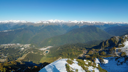 Panoramic view from the top of the Aibga mountain range to the ski resort Rosa Khutor. The valley is surrounded by high mountains with snowy slopes.