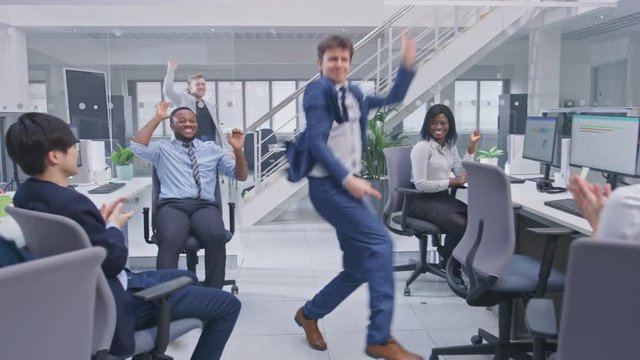 Young Happy Business Manager Wearing a Suit and Tie Dancing and Giving High Fives in the Office. Celebrating Success. Diverse and Motivated Business People Work on Computers in Modern Open Office.