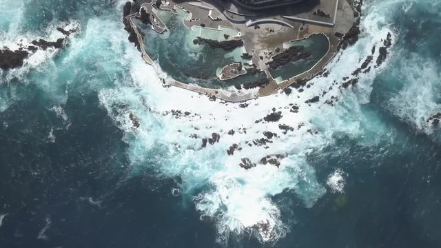 Big rough waves are hitting stones and walls of a natural swimming pool. It is the Atlantic Ocean in Madeira, Portugal. Beautiful water that shines blue with big power.