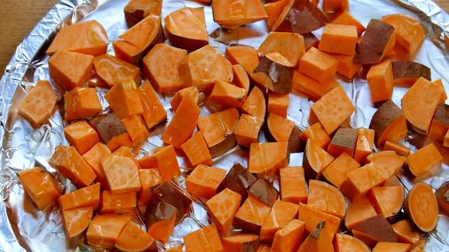 Cubed sweet potatoes getting seasoned before being put in the oven.