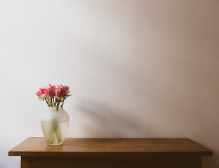 Pink and cream roses on wooden oak side table against neutral wall with moody lighting - warm matte filter effect and selective focus