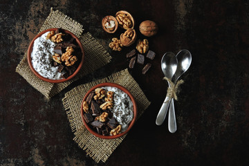 Two cups with yogurt with chia seeds, walnuts and dark chocolate. Breakfast or dessert for two. Healthy food. Keto diet. Diet recipes ideas. Shabby style. Dark background.