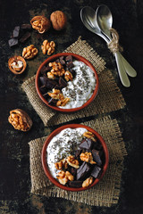 Two cups with yogurt with chia seeds, walnuts and dark chocolate. Breakfast or dessert for two. Healthy food. Keto diet. Diet recipes ideas. Shabby style. Dark background.