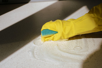 Hand in yellow rubber glove washing surface on a sunny day. Spring cleaning.brown color toned